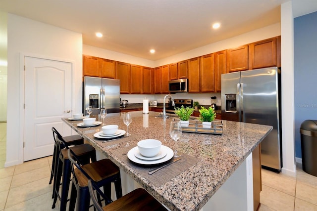 kitchen featuring light tile patterned floors, light stone counters, brown cabinets, stainless steel appliances, and recessed lighting