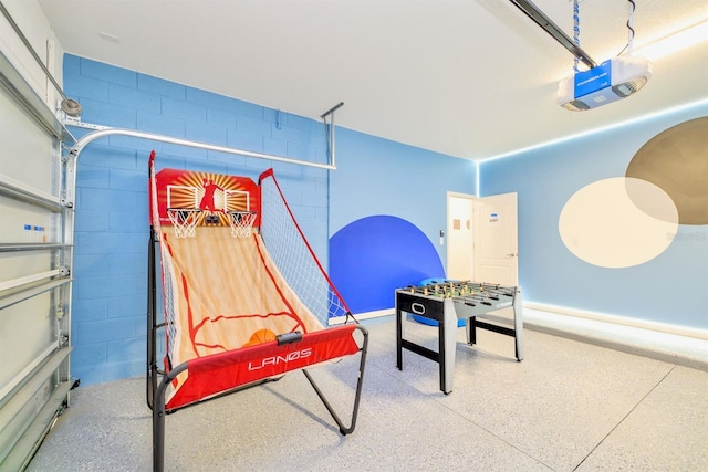 playroom with a garage, concrete block wall, and speckled floor