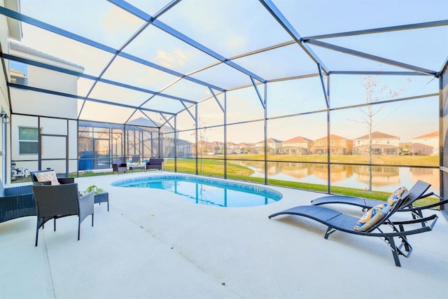 outdoor pool with glass enclosure, a patio area, and a water view