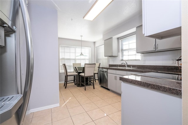 kitchen featuring light tile patterned floors, stainless steel appliances, a sink, backsplash, and dark countertops