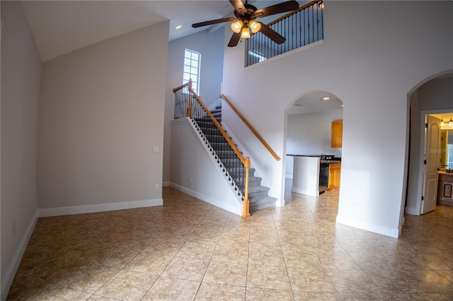 unfurnished living room with arched walkways, ceiling fan, high vaulted ceiling, baseboards, and stairway