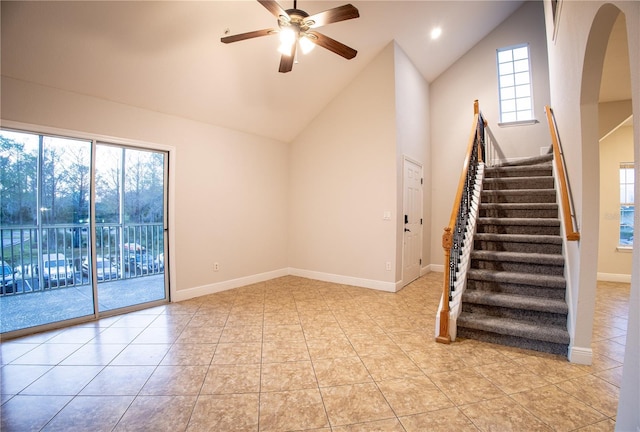 unfurnished room with arched walkways, light tile patterned floors, stairway, a ceiling fan, and baseboards