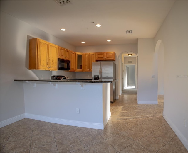 kitchen with arched walkways, a breakfast bar area, dark countertops, black microwave, and a peninsula