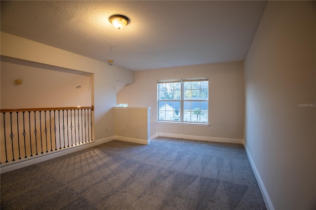 empty room featuring a textured ceiling, dark carpet, and baseboards