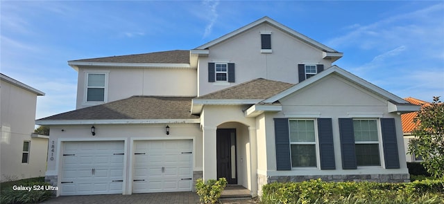 traditional-style home with an attached garage, stone siding, decorative driveway, roof with shingles, and stucco siding