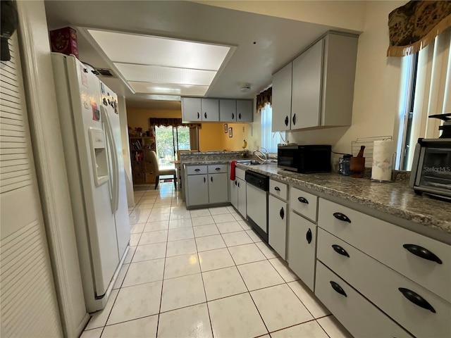 kitchen with light tile patterned floors, white appliances, dark countertops, and a sink