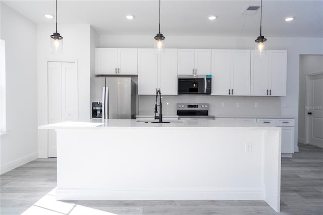 kitchen with a kitchen island with sink, a sink, light countertops, appliances with stainless steel finishes, and tasteful backsplash