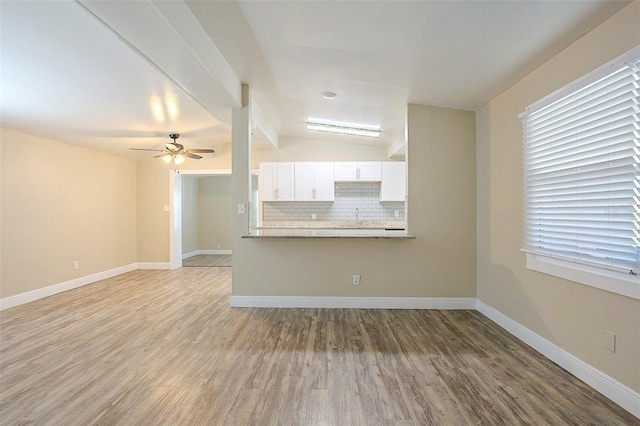 unfurnished living room featuring ceiling fan, baseboards, vaulted ceiling, wood finished floors, and a sink