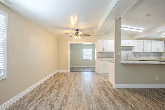 kitchen with baseboards, light wood finished floors, a sink, white cabinets, and tasteful backsplash