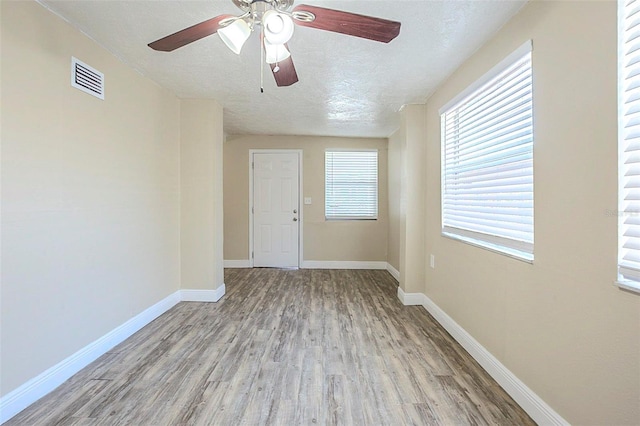 empty room with wood finished floors, visible vents, baseboards, and a textured ceiling