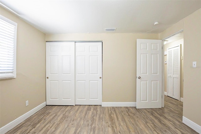 unfurnished bedroom with a closet, visible vents, baseboards, and wood finished floors