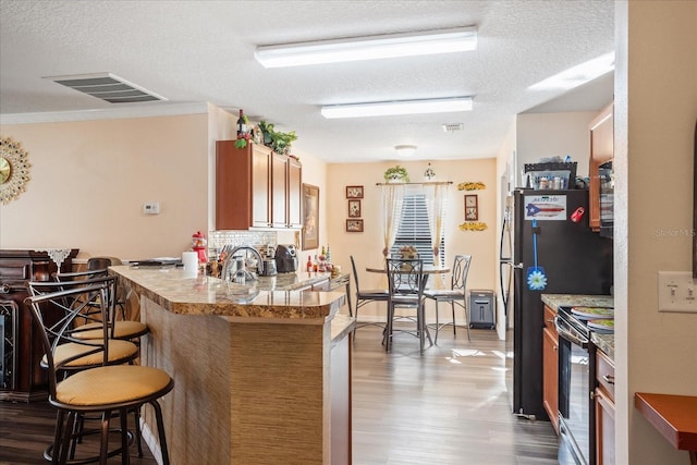 kitchen with visible vents, dark wood finished floors, a breakfast bar, a peninsula, and black electric range