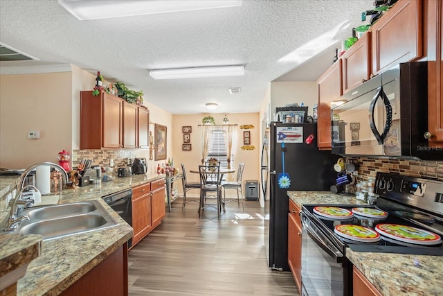 kitchen featuring a sink, visible vents, light wood-type flooring, black appliances, and tasteful backsplash