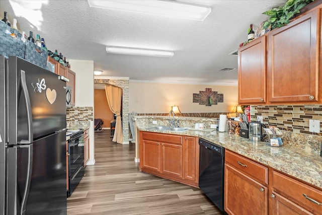 kitchen featuring decorative backsplash, light wood-style floors, a peninsula, black appliances, and a sink