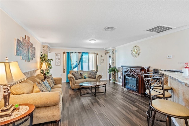 living area with dark wood-style floors, ornamental molding, a glass covered fireplace, and visible vents