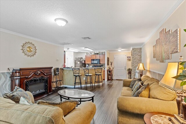 living room with visible vents, ornamental molding, wood finished floors, and a glass covered fireplace