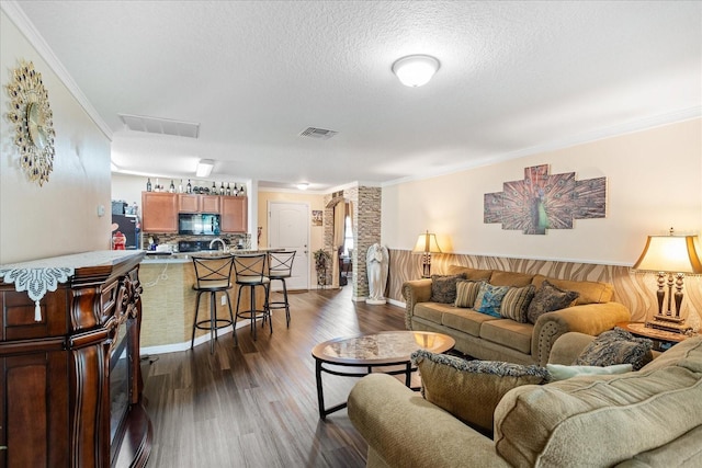 living area with dark wood-style floors, visible vents, crown molding, and a textured ceiling