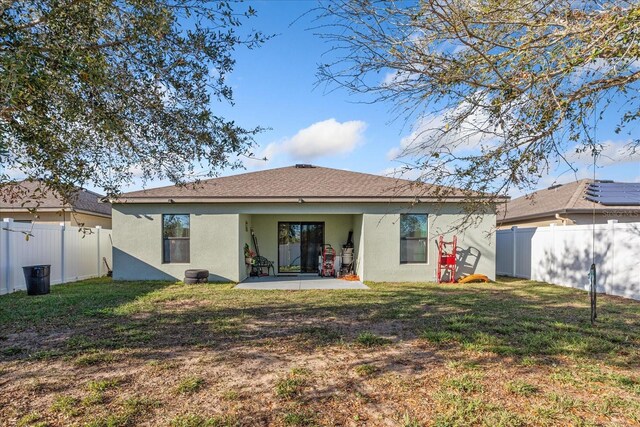 rear view of property with a yard, stucco siding, a shingled roof, a patio area, and a fenced backyard