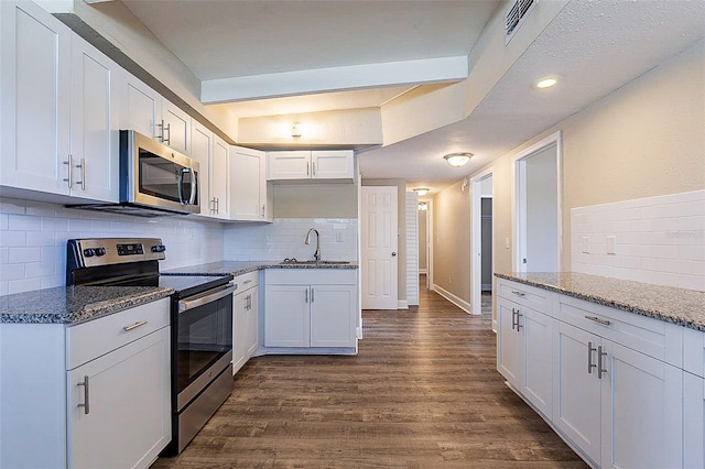 kitchen with dark stone countertops, appliances with stainless steel finishes, white cabinets, and dark wood-style flooring