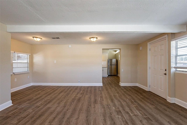 spare room featuring dark wood finished floors, visible vents, a textured ceiling, and baseboards