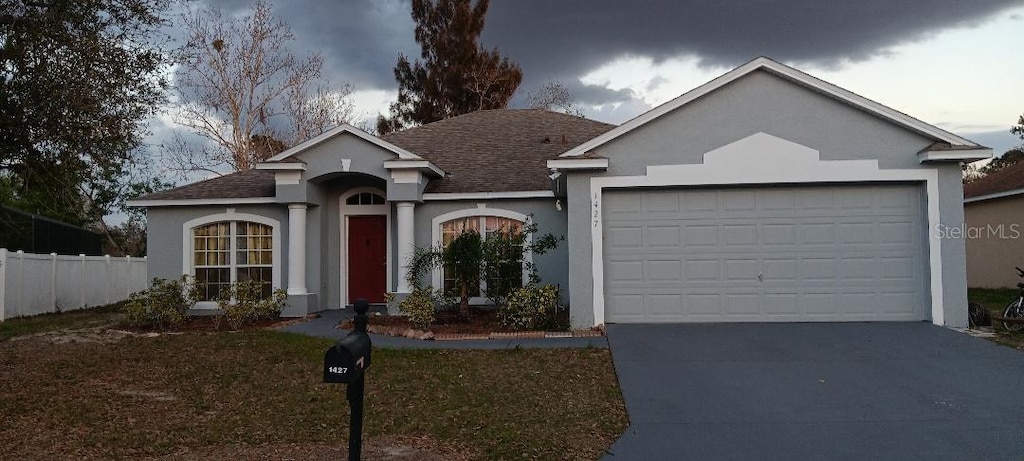 ranch-style home with concrete driveway, an attached garage, fence, and stucco siding