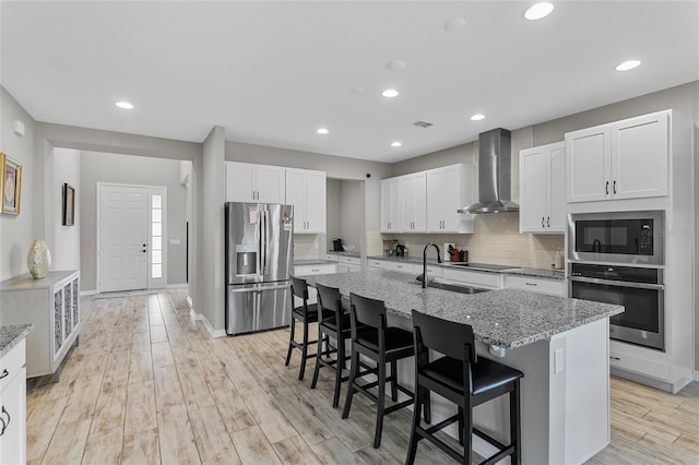 kitchen featuring a kitchen breakfast bar, white cabinets, appliances with stainless steel finishes, wall chimney range hood, and decorative backsplash