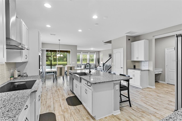 kitchen with a breakfast bar area, black electric stovetop, visible vents, a sink, and wall chimney range hood