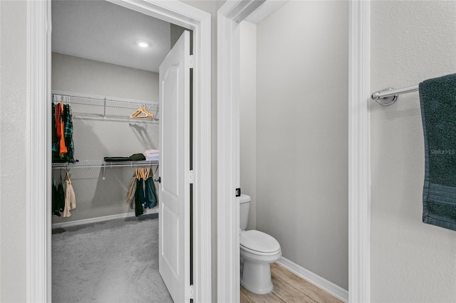 bathroom with toilet, baseboards, a walk in closet, and wood finished floors