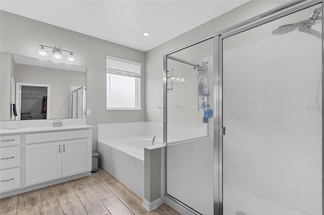 bathroom featuring wood finished floors, a garden tub, a walk in closet, vanity, and a shower stall