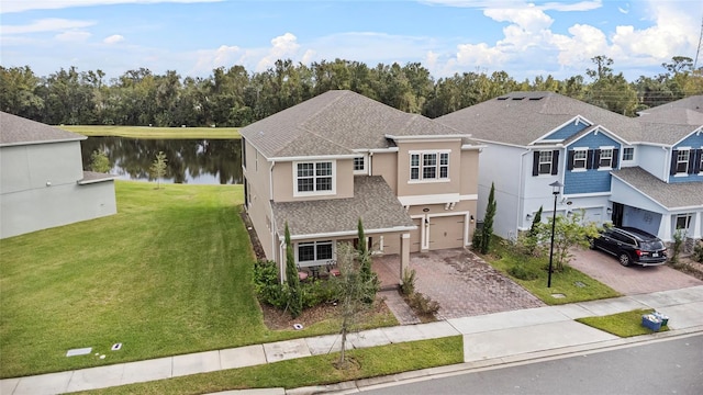 traditional home with a front lawn, decorative driveway, a water view, and stucco siding