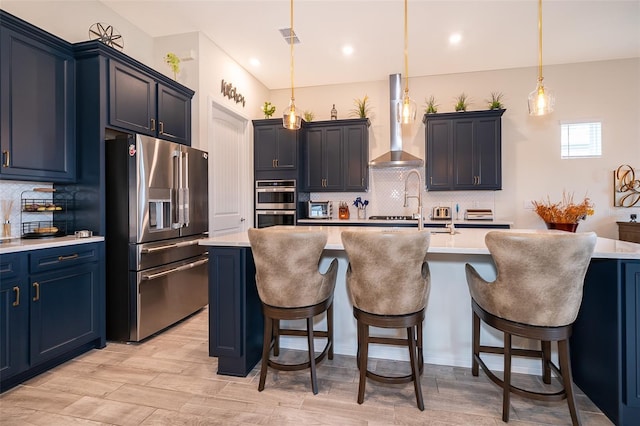 kitchen with stainless steel appliances, light countertops, wall chimney exhaust hood, and a kitchen bar