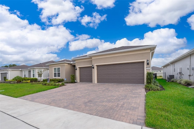 view of front of home featuring an attached garage, central air condition unit, decorative driveway, stucco siding, and a front yard