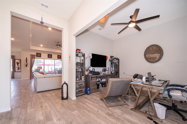 office area with a tray ceiling, visible vents, light wood-style floors, a ceiling fan, and baseboards