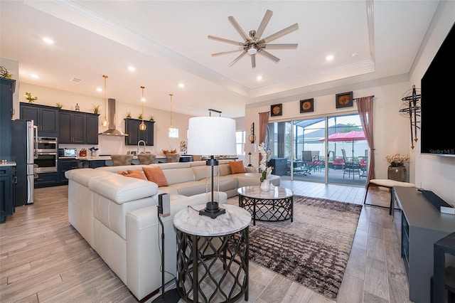 living room featuring recessed lighting, a raised ceiling, ornamental molding, ceiling fan, and light wood-type flooring