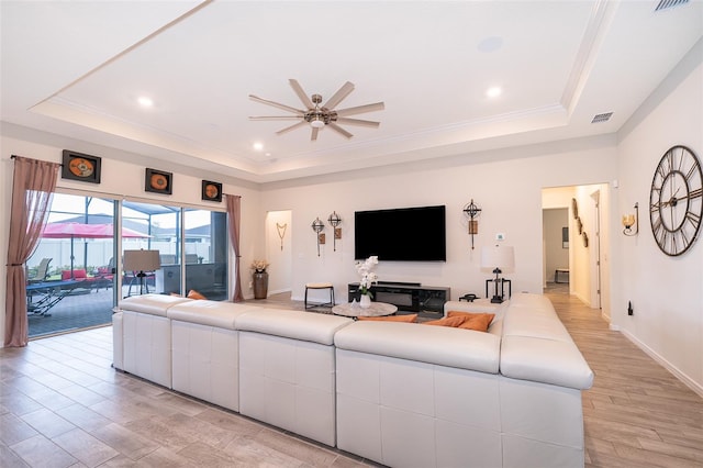 living area featuring ornamental molding, a raised ceiling, visible vents, and light wood-style flooring