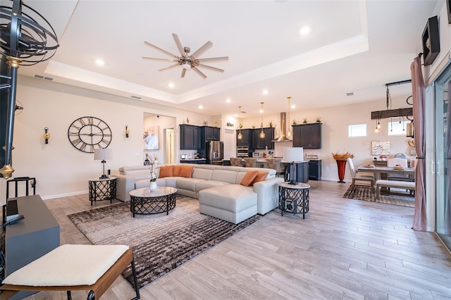 living area featuring light wood-style floors, a tray ceiling, visible vents, and crown molding