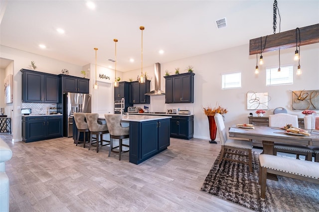 kitchen featuring stainless steel fridge, visible vents, wall chimney exhaust hood, a breakfast bar, and light countertops