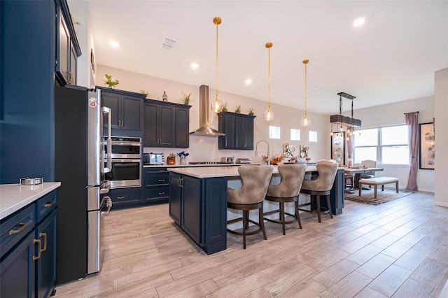 kitchen with visible vents, light countertops, appliances with stainless steel finishes, wall chimney exhaust hood, and a kitchen bar