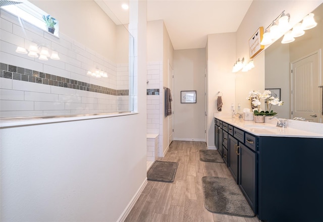 bathroom featuring a walk in shower, double vanity, wood finished floors, and a sink