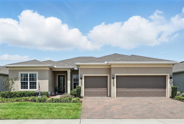 prairie-style house featuring stucco siding, a front yard, a garage, and decorative driveway