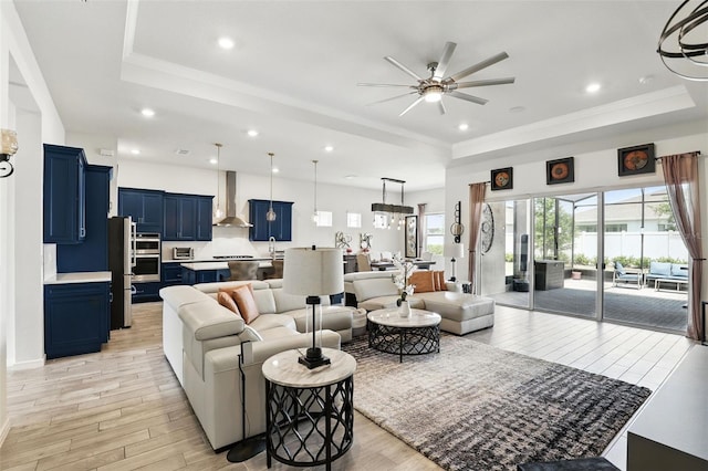 living area with ceiling fan, recessed lighting, a tray ceiling, and light wood-type flooring