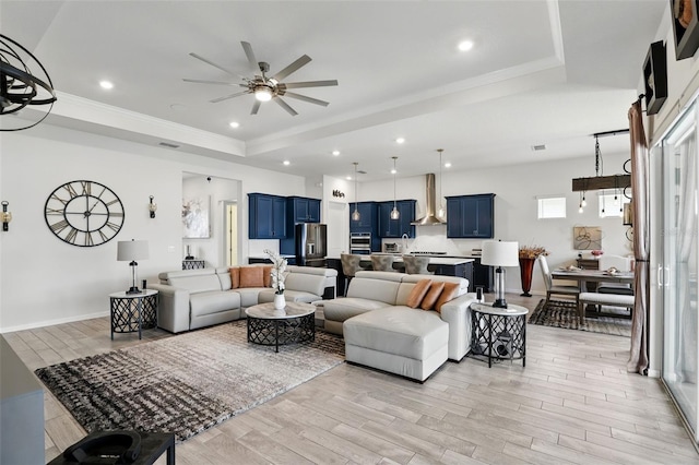 living room with a tray ceiling, light wood-style flooring, and ceiling fan