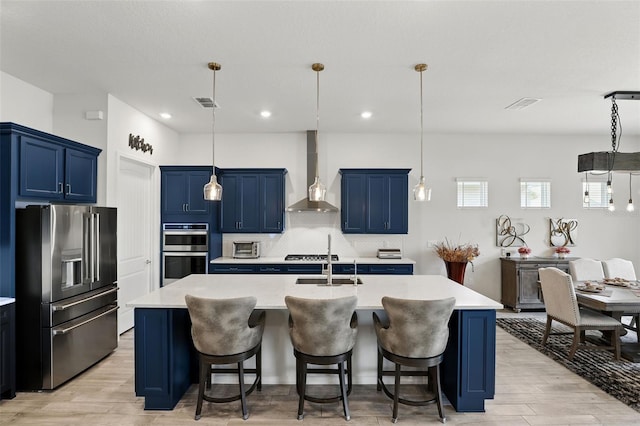 kitchen featuring blue cabinetry, wall chimney range hood, appliances with stainless steel finishes, and light countertops