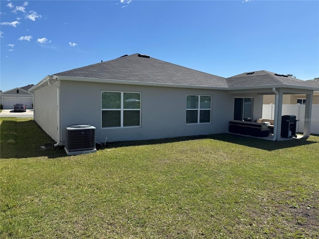 back of property featuring central AC unit, a shingled roof, fence, a lawn, and stucco siding