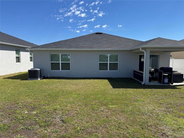 back of property with a shingled roof, cooling unit, a lawn, and stucco siding