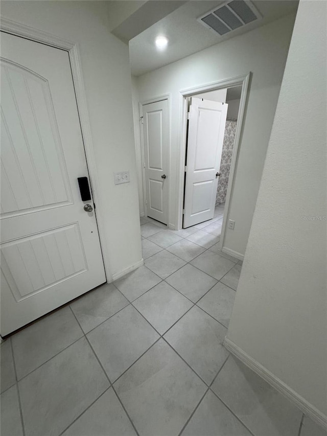 corridor with baseboards, visible vents, and light tile patterned flooring