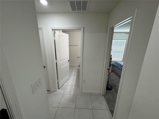 corridor featuring baseboards, visible vents, and light tile patterned flooring