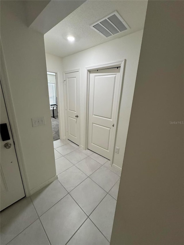 hall with light tile patterned floors, baseboards, visible vents, and a textured ceiling