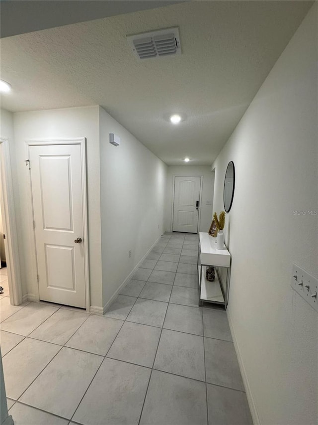 hall featuring light tile patterned floors, visible vents, and a textured ceiling