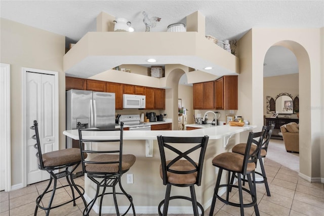 kitchen with a breakfast bar area, light countertops, a peninsula, brown cabinetry, and white appliances